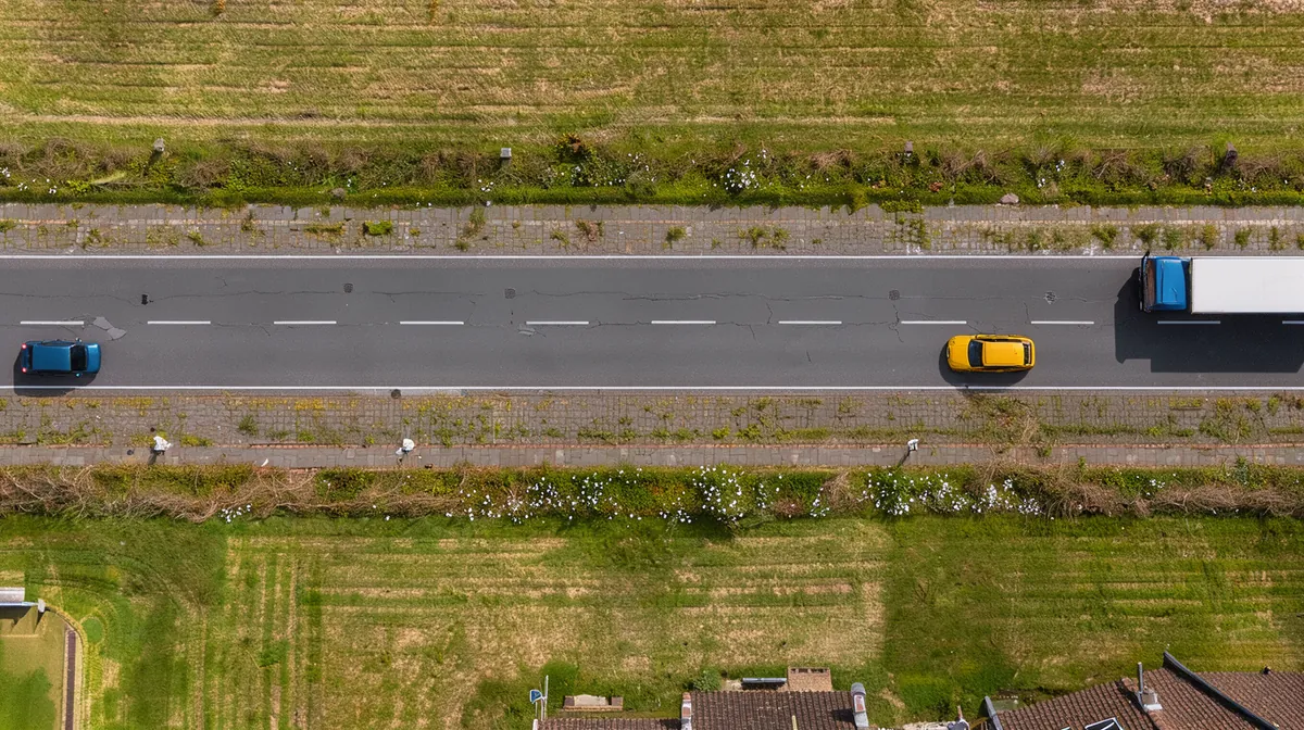 Bovenaanzicht van een landweg met twee rijstroken. Een vrachtauto rijdt de andere kant op. Een personenauto haalt die in en rijdt daarvoor op de weghelft van de eigen auto. De eigen auto houdt rechts en remt; een pijl wijst de ruimte naar rechts aan.